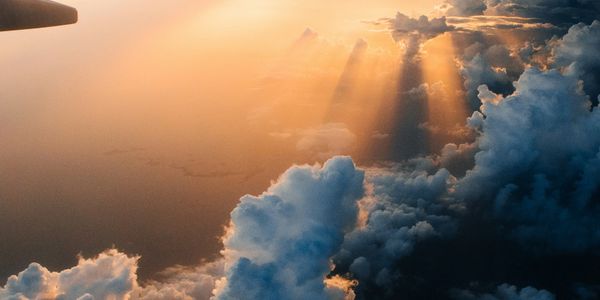 Golden sunlight beams through dense clouds during sunset from an airplane view.