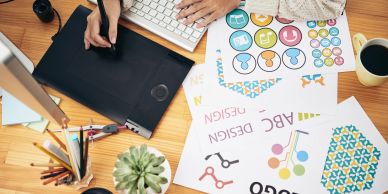 Person working on graphic design using a drawing tablet and colorful design sheets.