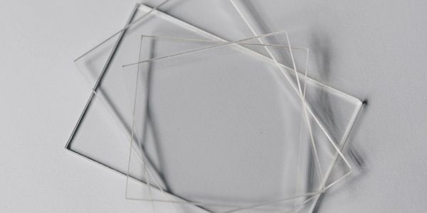 Several thin, transparent glass sheets overlapping on a light surface.
