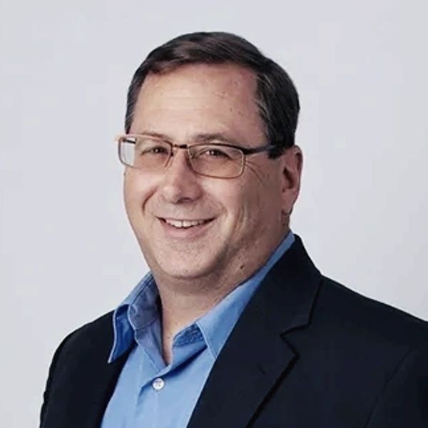 Smiling man in glasses and a blue shirt with a black blazer.