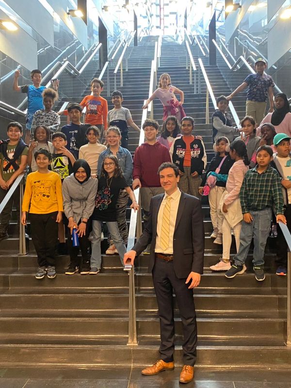 Group of children and a man posing on stairs indoors.