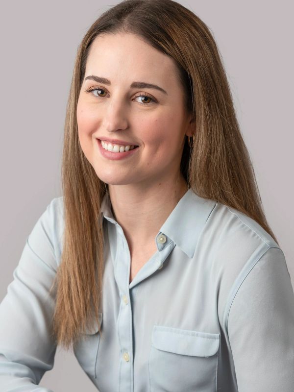 Smiling woman with long brown hair in light blue shirt.