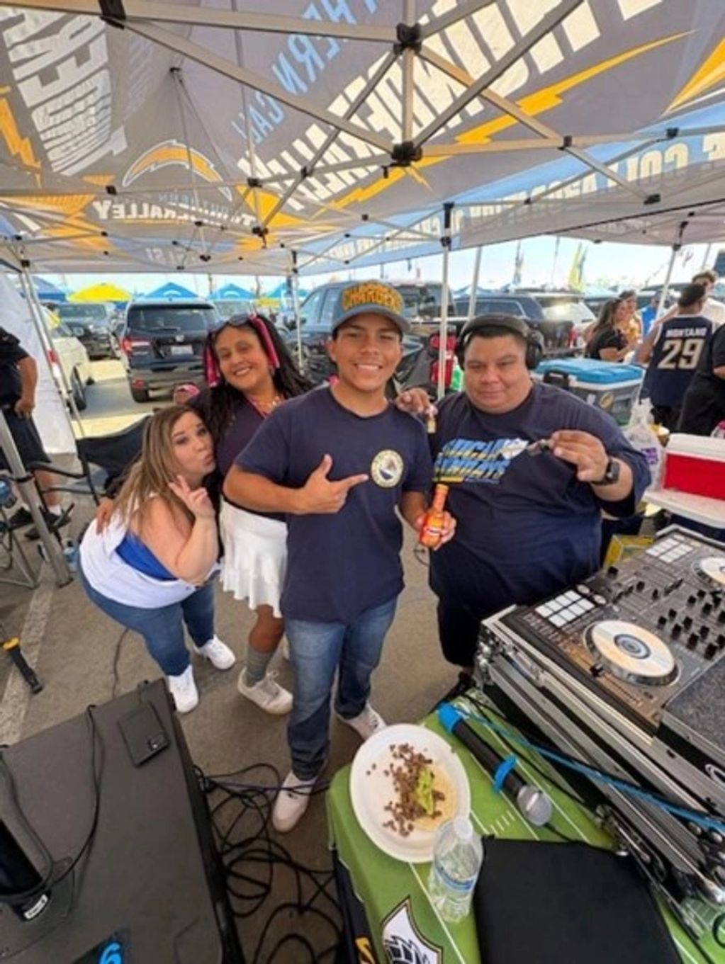 Group of friends enjoying a tailgate party with music and food under a Chargers tent.