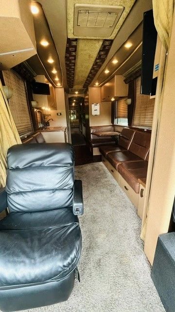 Interior of a well-lit luxury RV with leather seating and carpeted floor.