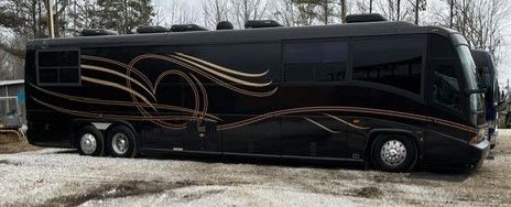 A sleek black luxury motorhome with gold swirls parked on gravel.