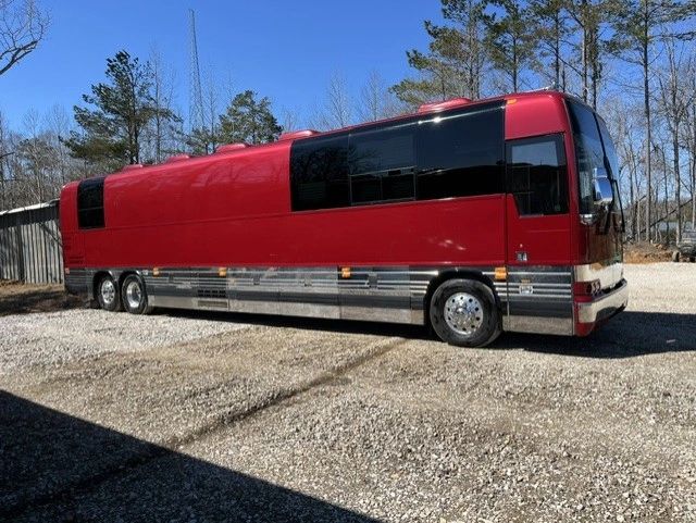 A sleek red tour bus parked on a gravel lot under a clear blue sky.