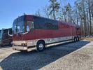 A long, red limousine parked on gravel near trees.
