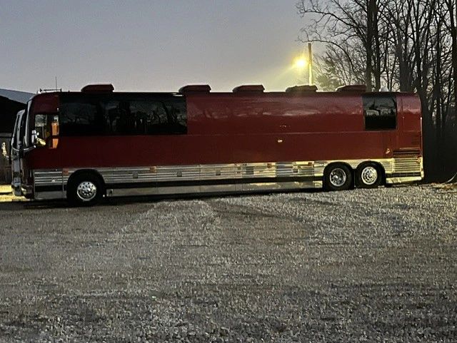 A large red motorhome parked on gravel at dusk with trees in the background.