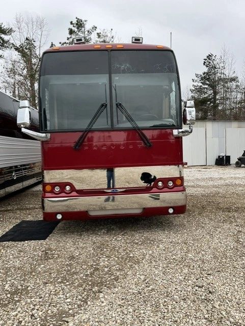 Front view of a red and silver luxury bus parked on gravel.