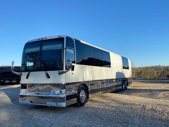 White and silver luxury tour bus parked on gravel with clear blue sky.