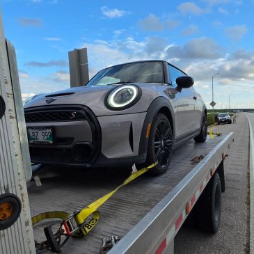 Mini Cooper on a tow truck under a cloudy sky.