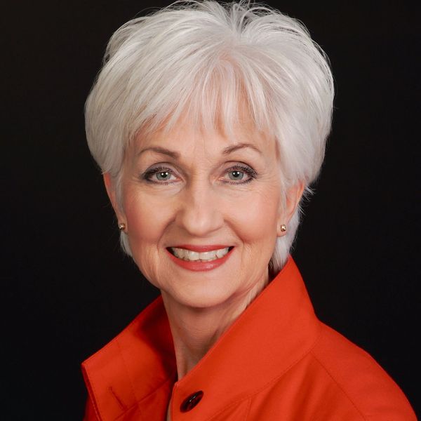 Smiling elderly woman with white hair wearing a bright orange jacket.