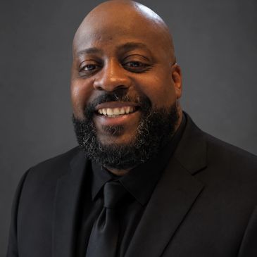 Smiling man in a black suit with a black background.