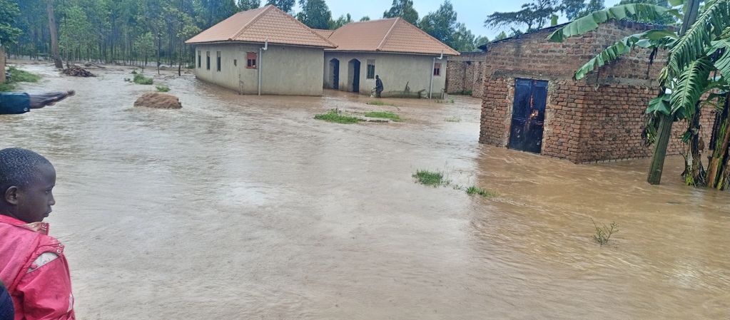 Floodwater surrounds houses and trees in a rural area with people observing.