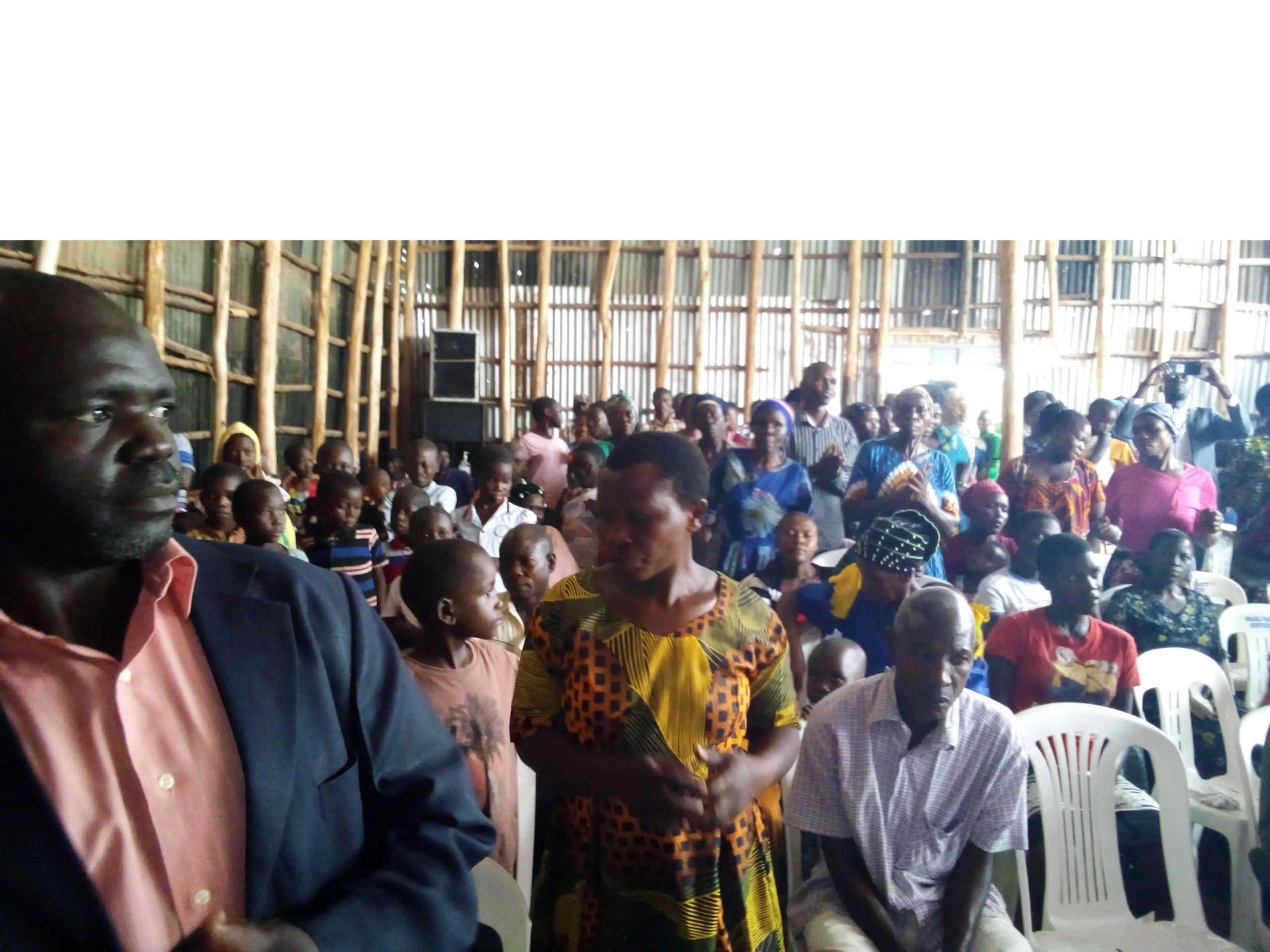 A group of people gathered inside a wooden structure, some standing and some seated.