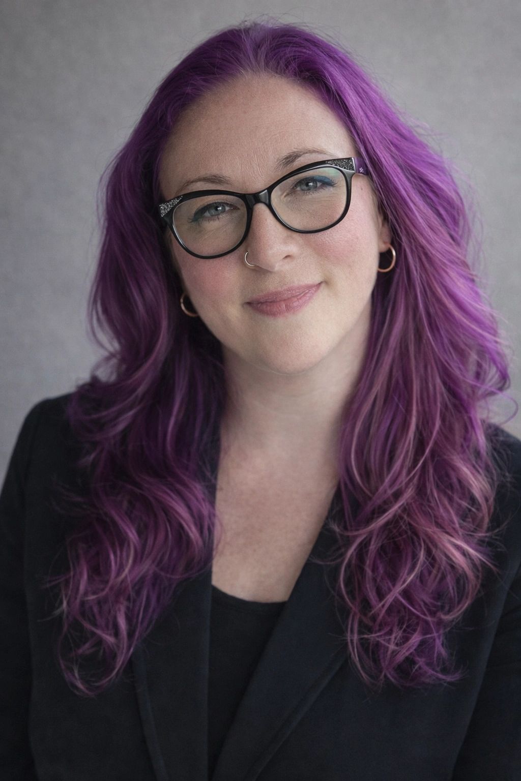Woman with purple hair and glasses smiling warmly.