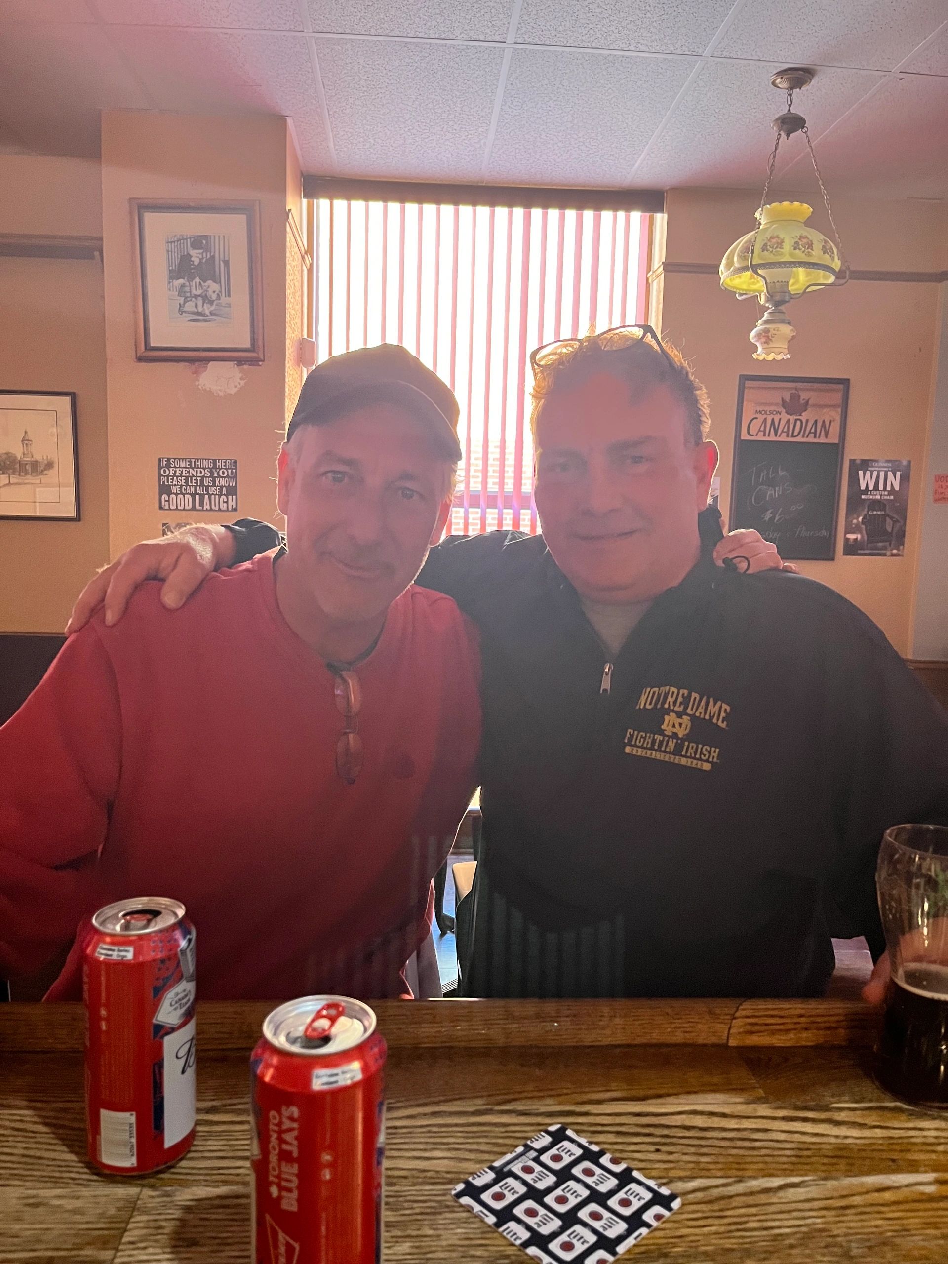 Two men sitting at a bar with drinks, smiling for a photo.
