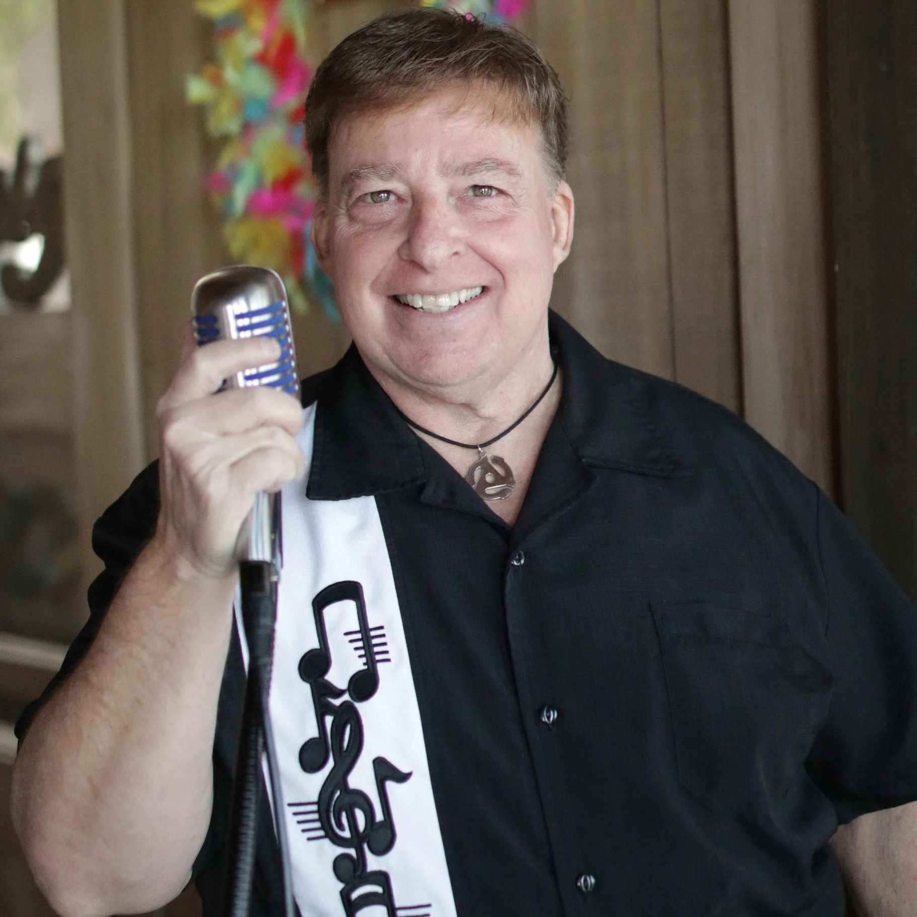 Man holding vintage microphone with musical notes sash.