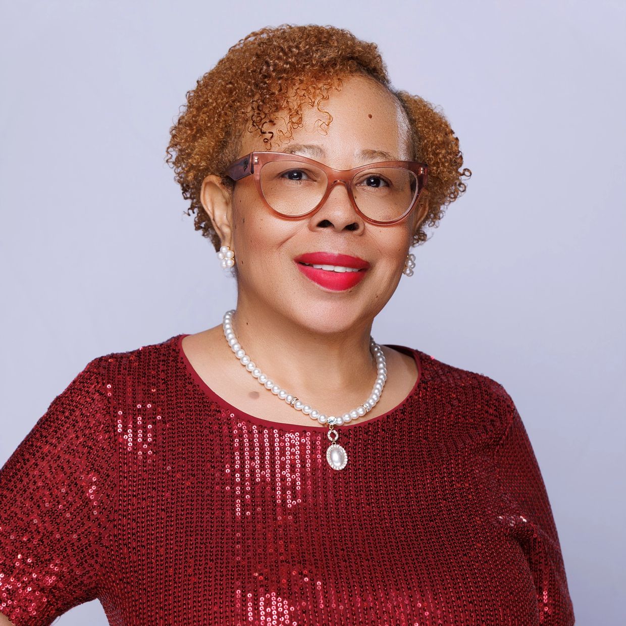Smiling woman wearing glasses, pearl necklace, and a red sequined top.
