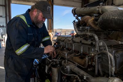 A mechanic working on a large engine inside a workshop.