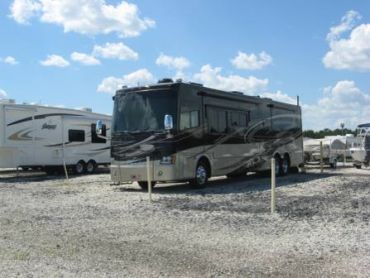 Large black motorhome parked on gravel under blue sky.