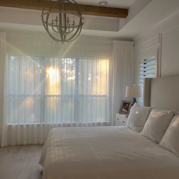 Sunlight fills a cozy, white bedroom with sheer curtains.