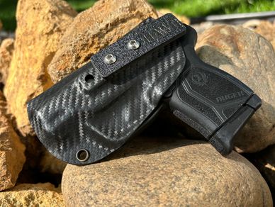 A Ruger handgun partially covered by a carbon fiber holster resting on rocks.