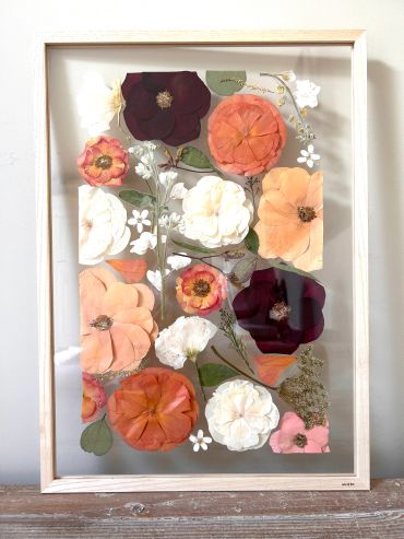 Pressed flowers art piece in a light wooden frame.