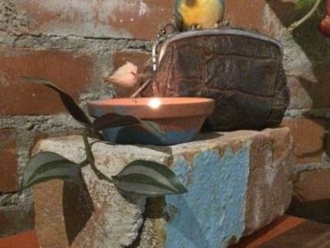 A brown clay candle holder with a lit candle on a stone platform.
