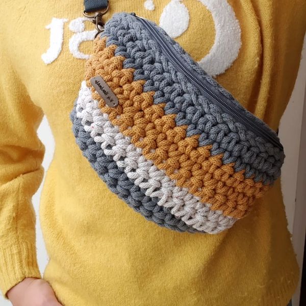 Crocheted fanny pack worn over a yellow sweater.