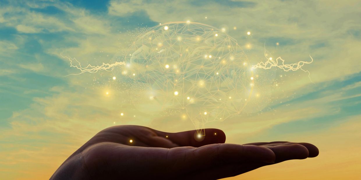 Hand holding a glowing digital brain with electric sparks.