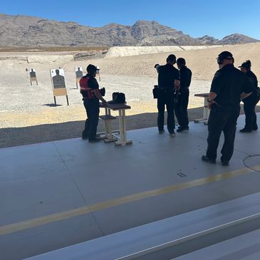 People at an outdoor shooting range with targets and mountains in the background.