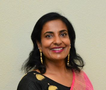 A smiling woman in traditional attire with gold earrings.