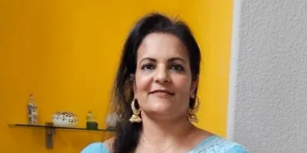 Woman in a blue outfit standing against a yellow and gray wall.