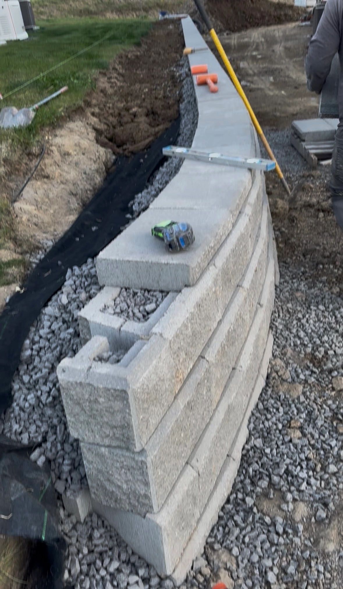 Curved retaining wall under construction with tools placed on top and gravel base.