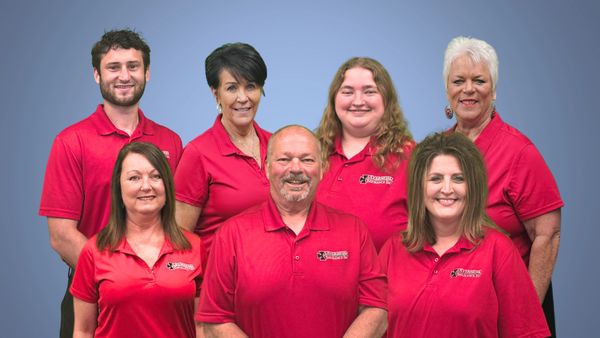 A group of seven people in matching red polo shirts posing against a blue background.