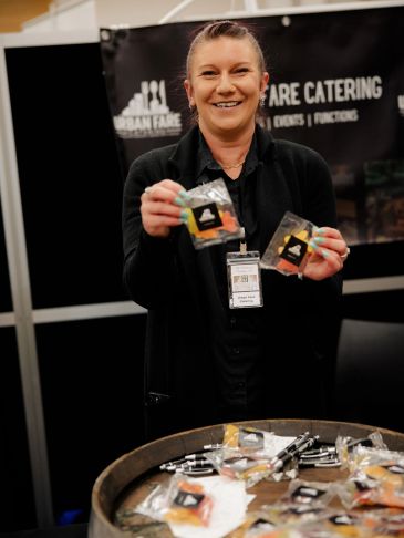 Smiling woman presenting packaged food items at a catering booth.