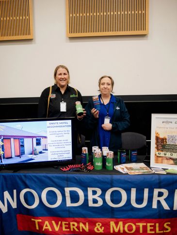 Two women standing behind a Woodbourne Tavern &amp; Motels booth.