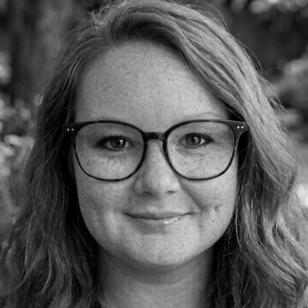 Close-up portrait of a smiling woman with glasses and wavy hair.