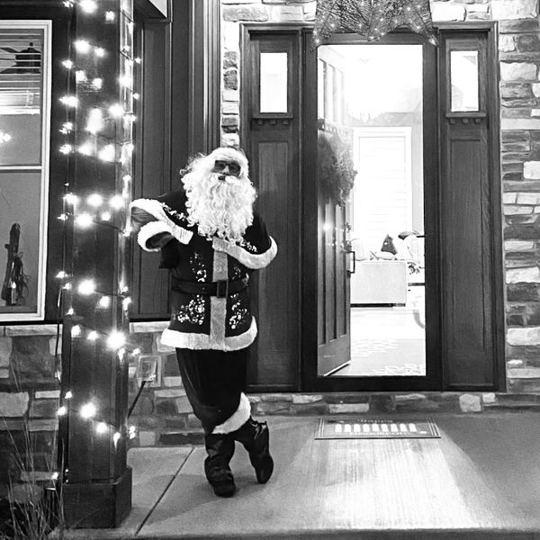 Santa Claus figure posing outside a decorated front door with lights.