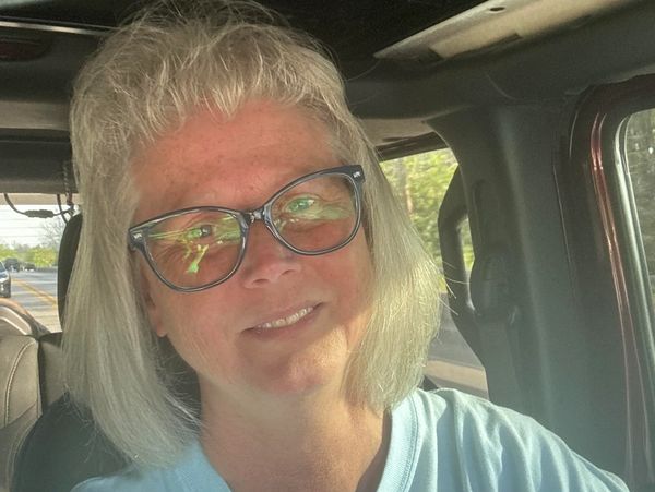 Woman with glasses smiling inside a car with sunlight on her face.