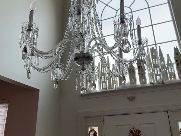 Elegant crystal chandelier hanging in a bright entryway with decorative miniature houses on the window sill.