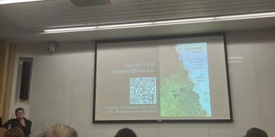 Presenter showing a slide with a QR code and a map in a classroom.