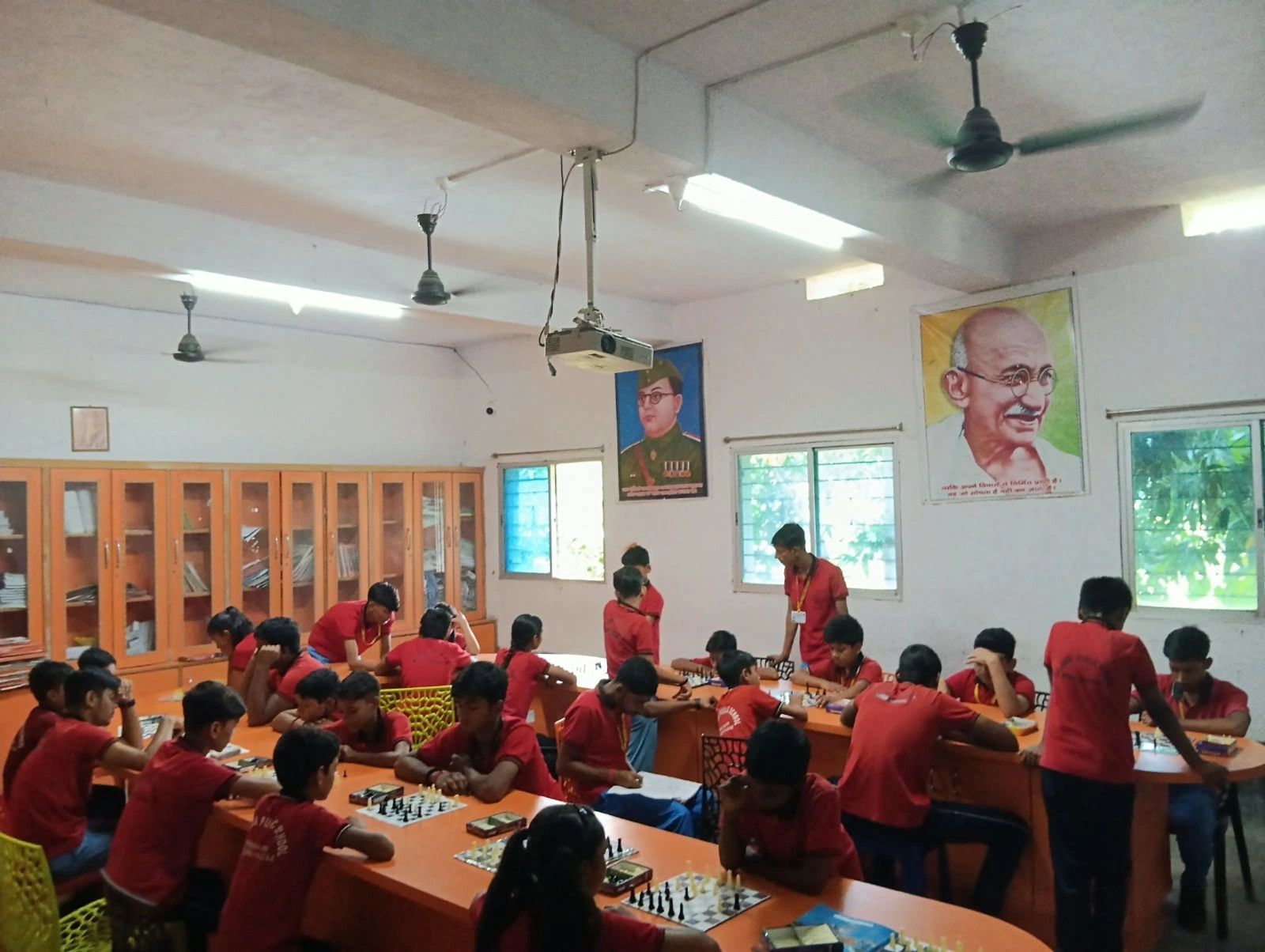 Students playing chess in a classroom with portraits on the wall.
