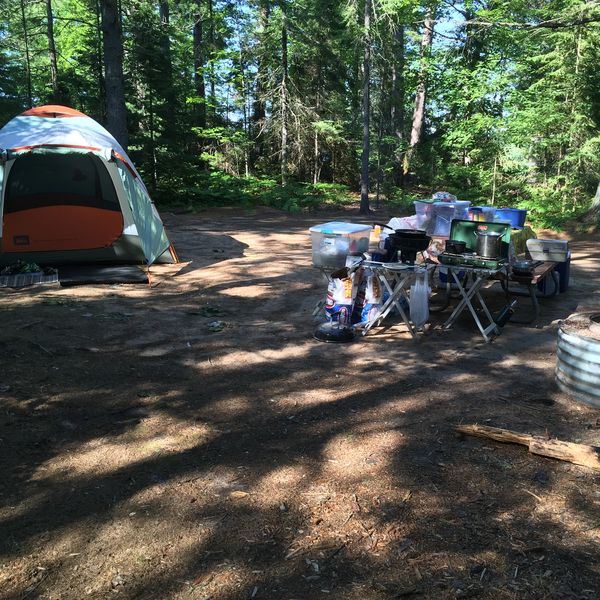 Tent at a rustic campsite, a picnic table has a camp stove and cooking utensils on it.