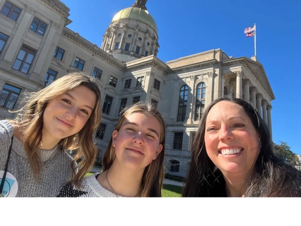 Three women smiling in front of a historic government building with a golden dome.