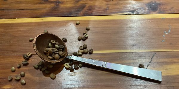 Metal spoon with coffee beans scattered on a wooden table.