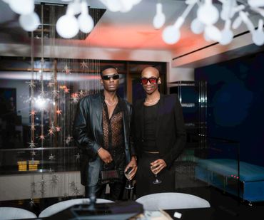 Two stylish men posing indoors at a modern, upscale venue.