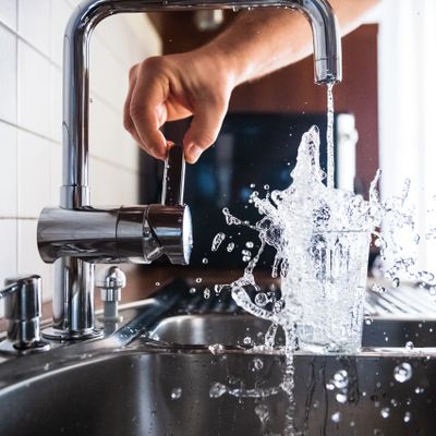 Hand turning off a kitchen tap as water splashes from a glass.