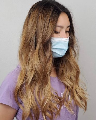 Woman with long wavy blonde hair wearing a face mask and purple shirt.